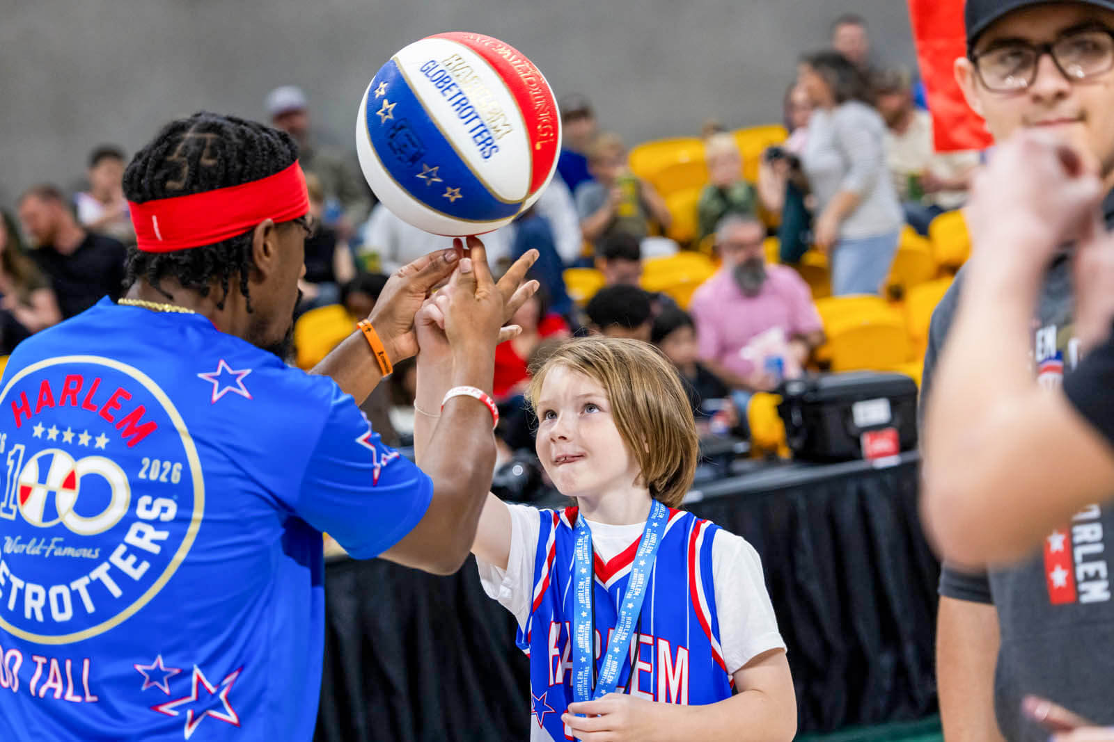 A Harlem Globetrotter helps a young child spin a basketball on their finger